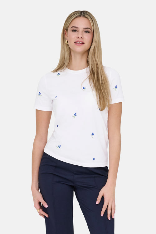 T-shirt blanc à manches courtes de ONLY, orné de motifs floraux bleus, porté avec un pantalon marine.
