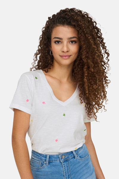 T-shirt blanc à col V de ONLY, orné de broderies de trèfles colorées et porté avec un jean.
