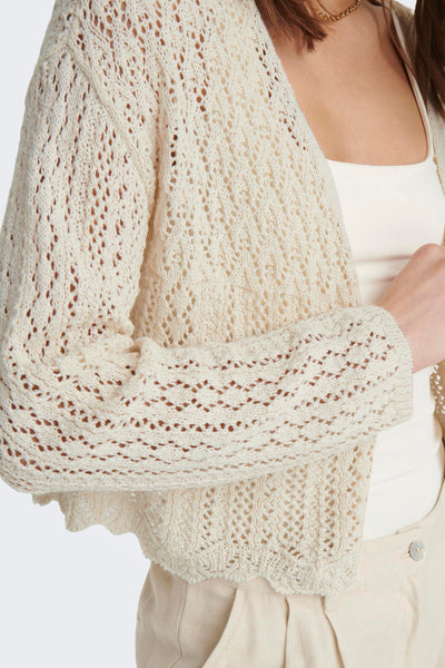 Ecru gebreid vest met open structuur van ONLY, gedragen met een hemdje en een beige broek.