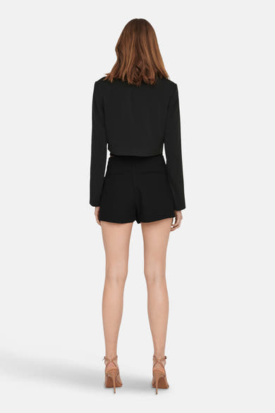 Zwarte korte rok van ONLY® met een bijpassend zwart kort jasje, van achteren gezien en beige hakken.