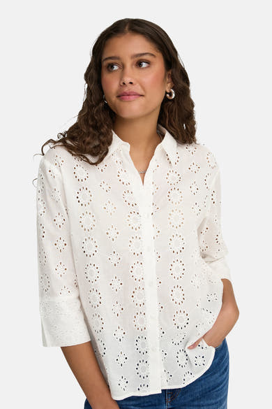 Wit overhemd met lange mouwen van JDY, ajourbroderie met bloemenpatroon, gedragen met een blauwe jeans en zilveren oorbellen.