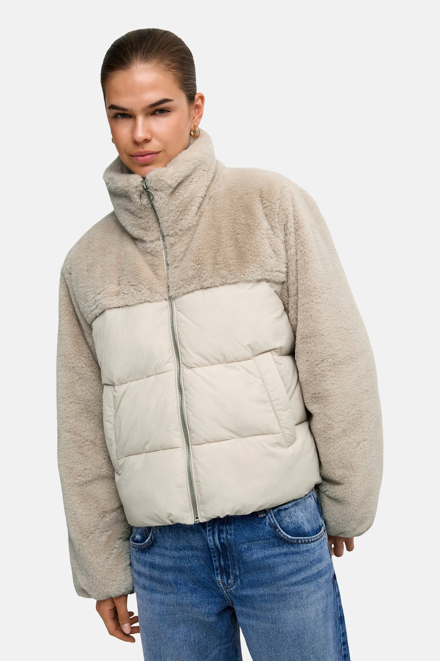 Beige and cream two-tone quilted puffer jacket with faux shearling collar and sleeves, worn with blue jeans, front view