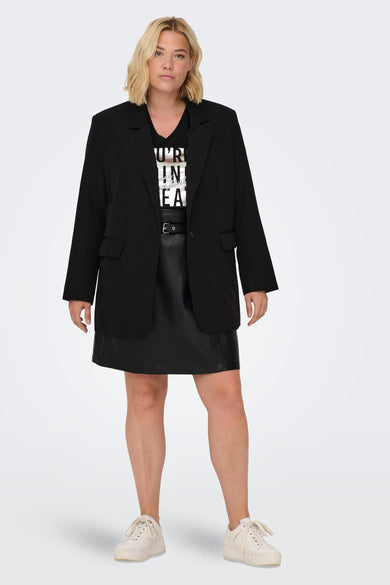 Blazer noir de CARMAKOMA, porté avec un t-shirt imprimé, une jupe en cuir et des baskets compensées.