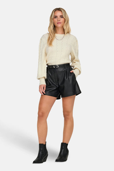 Pull à col rond beige de ONLY®, porté avec un short noir en similicuir et des bottines noires.
