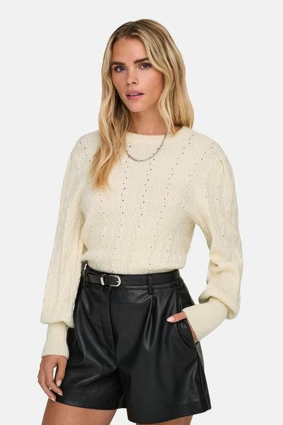 Pull beige à col rond de ONLY®, à motif texturé porté avec un collier et un pantalon en cuir noir.
