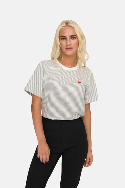 T-shirt à manches courtes gris rayé de JDY, orné d'un petit cœur rouge et porté avec un pantalon noir.
