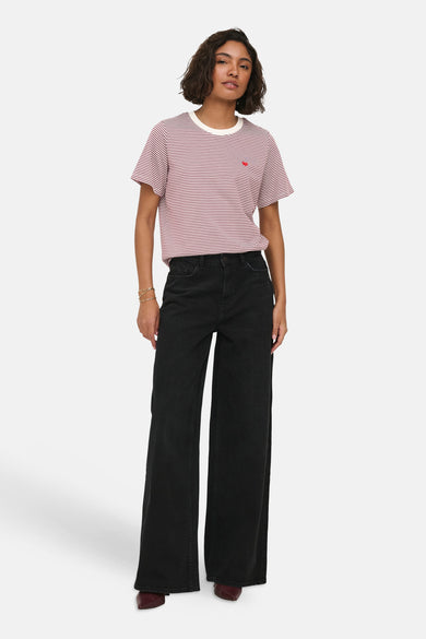 Red and white striped short-sleeve t-shirt with chest pocket and small red heart detail, worn with black wide-leg jeans and burgundy boots, front view.