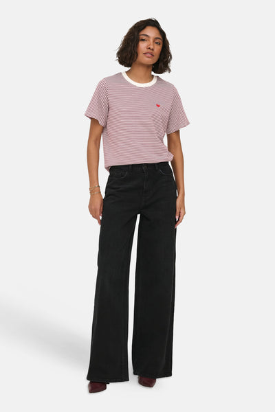 Red and white striped short-sleeve t-shirt with chest pocket and small red heart detail, worn with black wide-leg jeans and burgundy boots, front view.