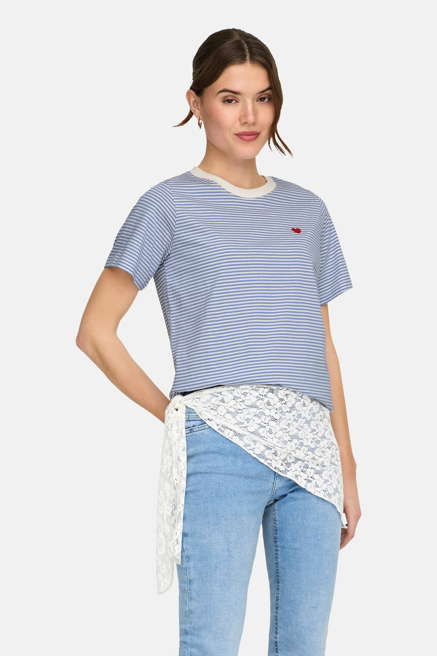 T-shirt à manches courtes bleu à rayures by JDY, avec un petit cœur rouge sur la poitrine, porté avec un jean et une ceinture en dentelle.
