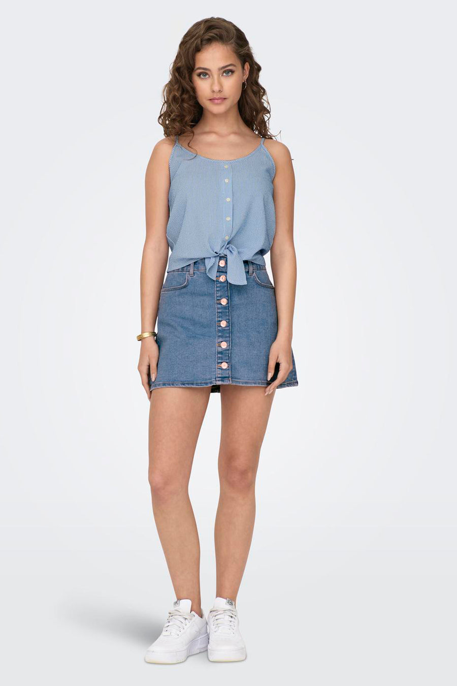 Chemisier bleu sans manches de ONLY, rayé, noué à la taille, porté avec une jupe en jean et des baskets blanches.