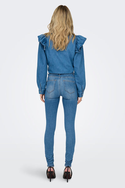 Blue skinny jeans from back view, mid-rise with slim fit, worn with denim top and black heels