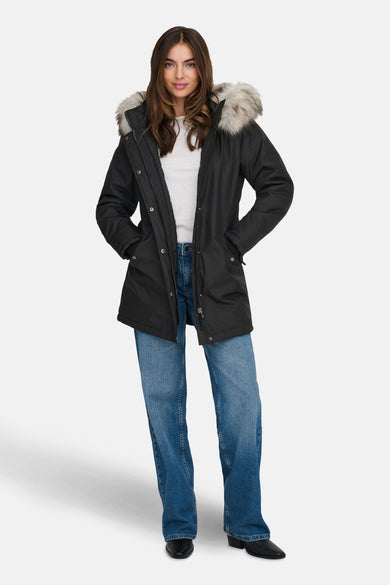 Veste longue noire de ONLY, avec capuche bordée de fourrure, portée avec un jean bleu et des bottines noires.