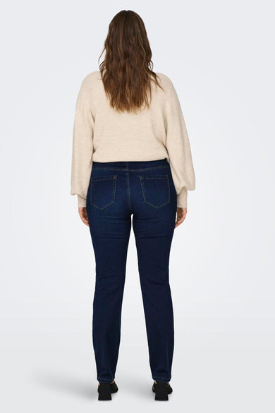 Jean droit bleu de CARMAKOMA, avec des poches arrière et porté avec un pull beige.