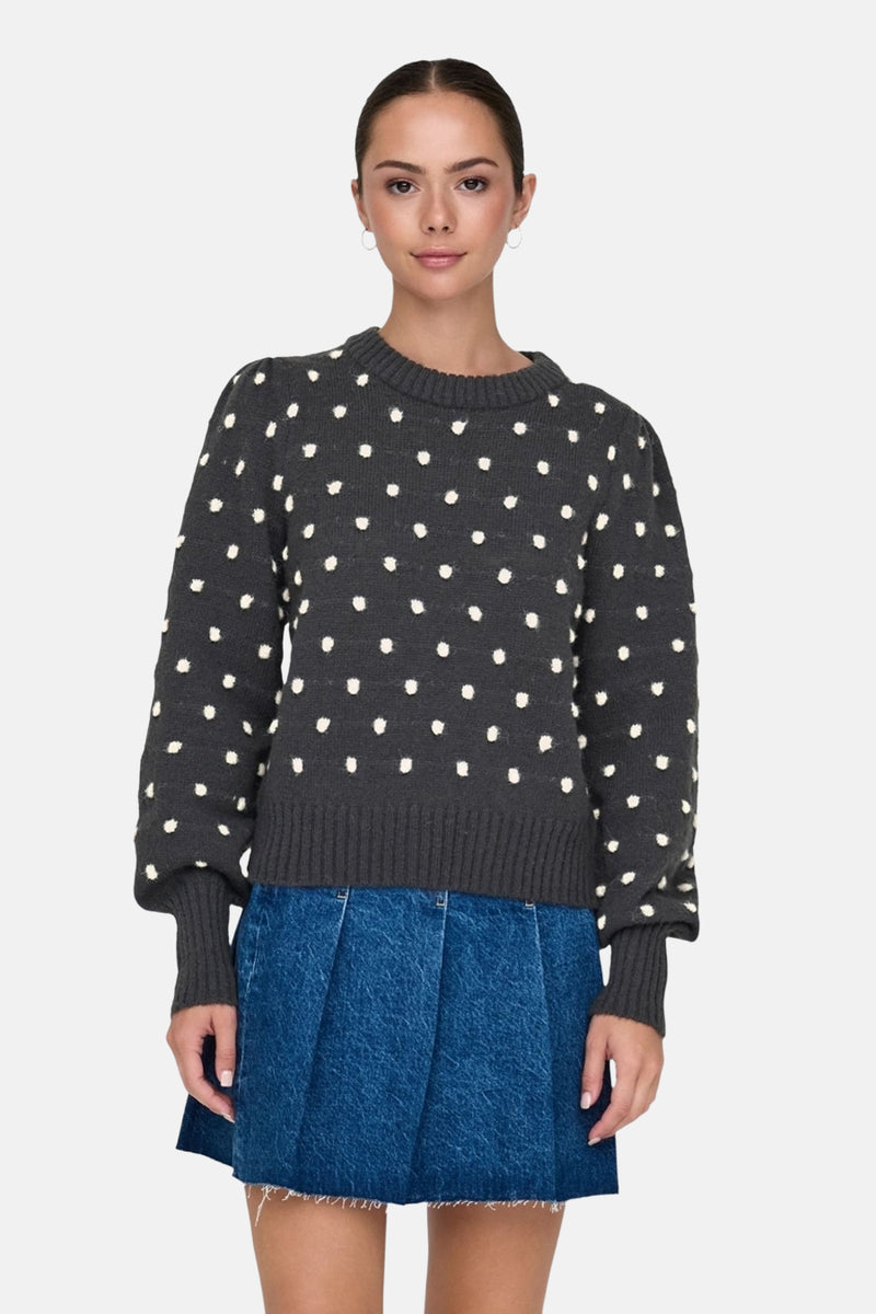Pull à col rond gris de JDY avec motif à pois blancs, porté avec une jupe bleue.
