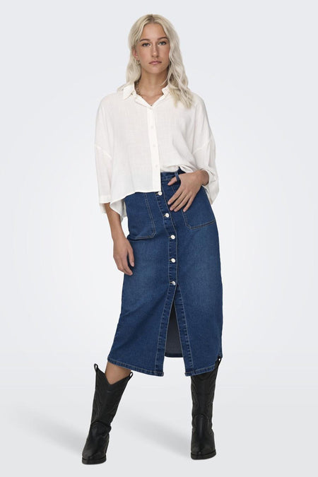 Chemise écru à manches longues de ONLY, portée avec une jupe en jean boutonnée et des bottes noires.