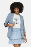 Blauwe ONLY® blazer, driekwartmouwen opgerold, gedragen over een T-shirt met bloemenprint en een bijpassende rok.