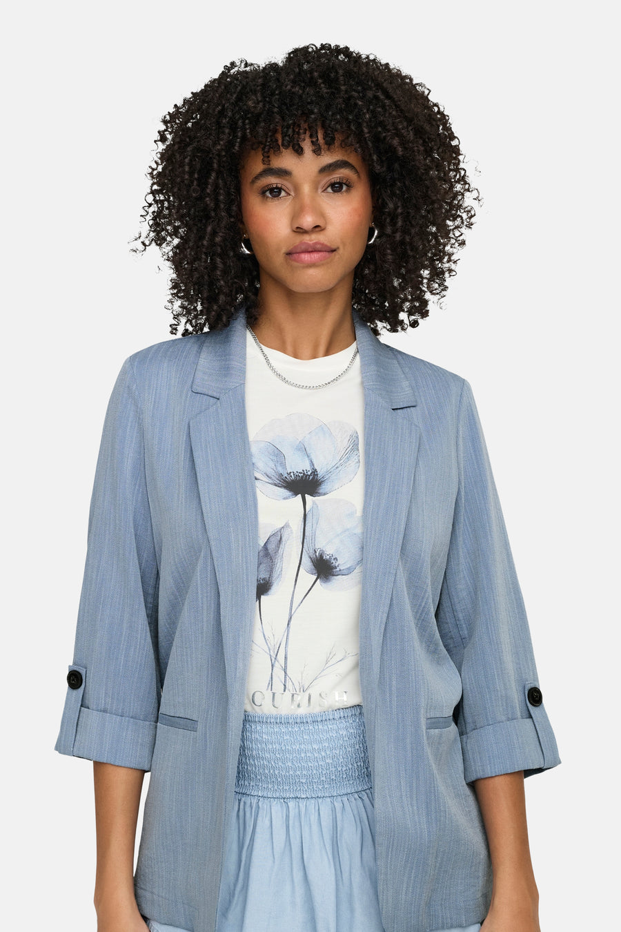 Blauwe blazer van ONLY, met driekwartmouwen en knopen bij de manchetten, gedragen over een T-shirt met bloemenprint.