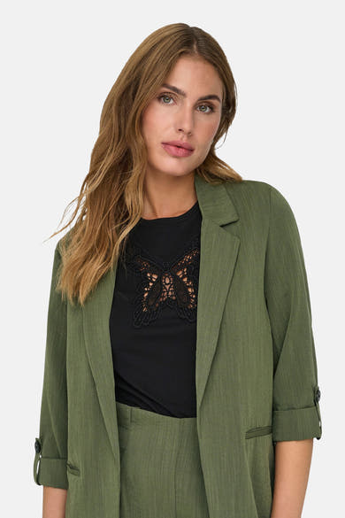 Olijfgroene blazer van ONLY, met driekwartmouwen die opgerold zijn en een zwart overhemd met vlinderprint.
