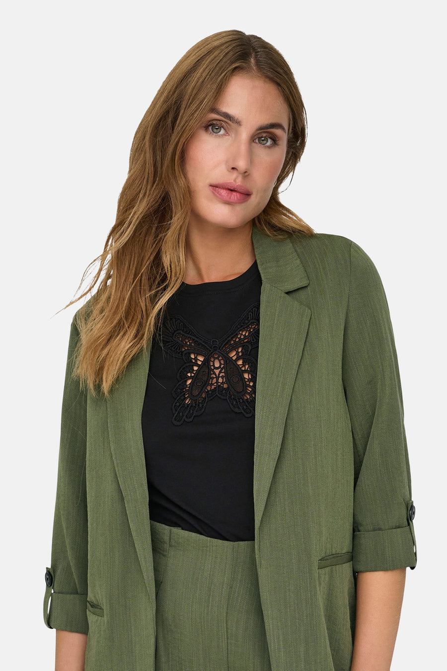 Olijfgroene blazer van ONLY, met driekwartmouwen die opgerold zijn en een zwart overhemd met vlinderprint.