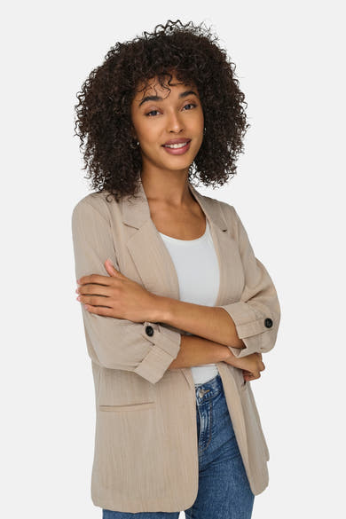 Blazer beige de ONLY, porté sur un t-shirt blanc et un jean, avec les bras croisés.