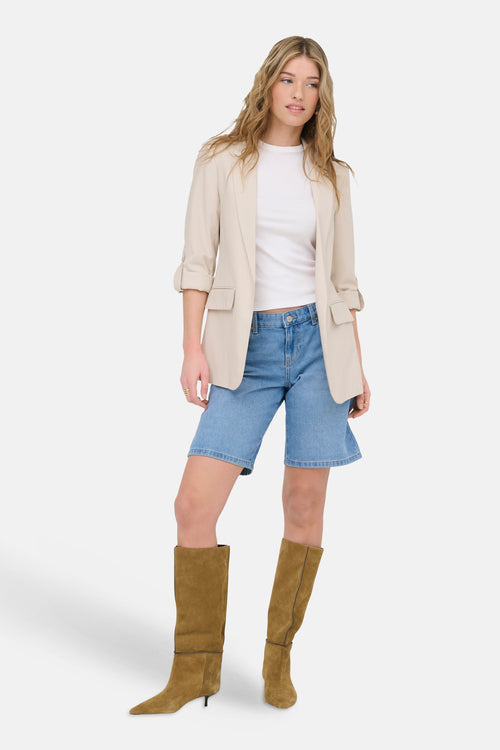 Blazer beige de ONLY®, porté avec un t-shirt blanc, un short en jean et des bottes hautes marron.