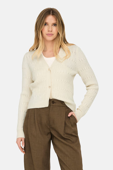Cardigan beige de ONLY, avec boutons décoratifs en forme de cœur, porté sur un t-shirt et un pantalon marron.
