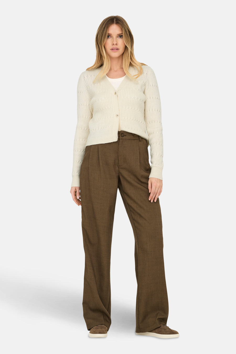 Cardigan beige en maille par ONLY®, porté avec un pantalon marron taille haute et des chaussures de sport.

