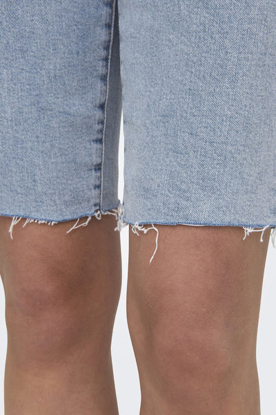 Short en denim bleu délavé de ONLY, avec ourlet effiloché et jambes partiellement visibles.