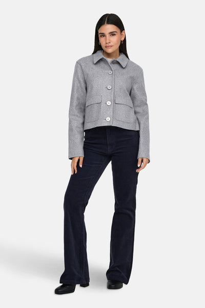 Kort grijs jasje van JDY, met opgestikte zakken en knopen aan de voorkant, gedragen met een corduroy broek.