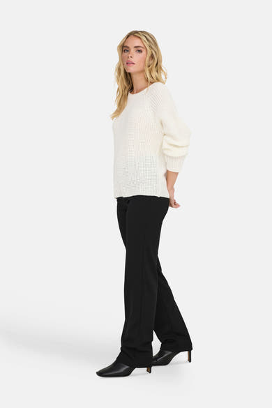 Pull à col rond blanc de JDY, à mailles apparentes, porté avec un pantalon noir et des bottines.
