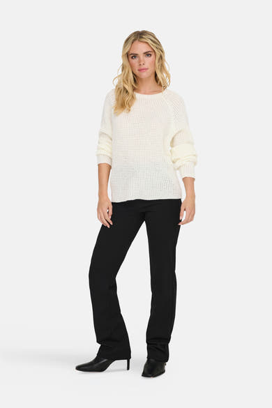 Pull à col rond blanc de JDY, en maille ajourée, porté avec un pantalon noir et des bottines noires.
