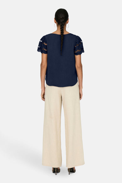 T-shirt bleu à manches courtes de JDY, avec détail ajouré sur les manches et porté avec un pantalon beige.