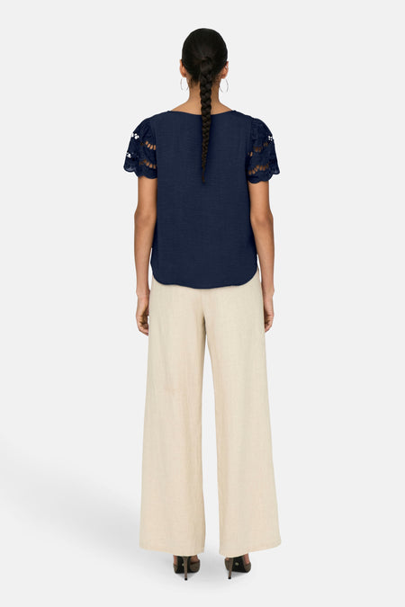 T-shirt bleu à manches courtes de JDY, avec détail ajouré sur les manches et porté avec un pantalon beige.