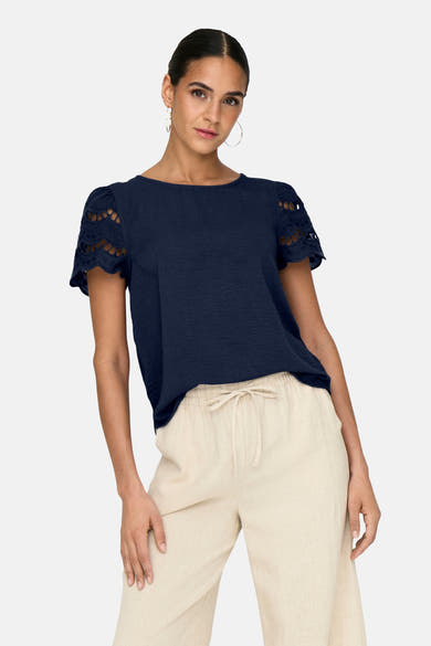 T-shirt bleu à manches courtes de JDY, avec détails ajourés aux manches et porté avec un pantalon beige.