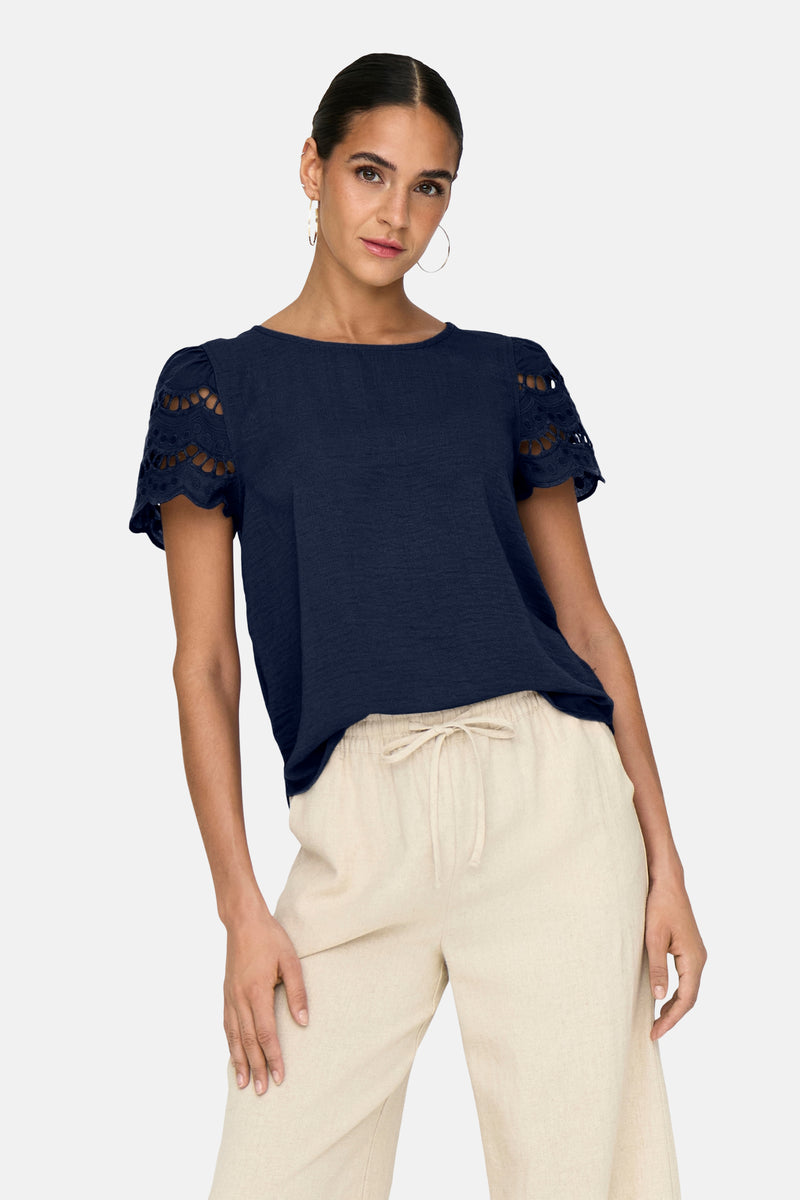 T-shirt bleu à manches courtes de JDY, avec détails ajourés aux manches et porté avec un pantalon beige.