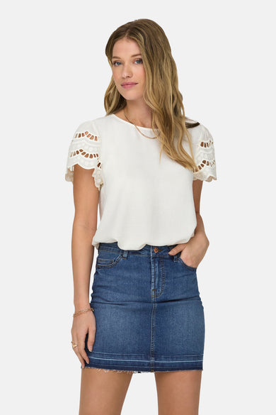 Ecru T-shirt met korte mouwen van JDY, met uitgesneden details op de mouwen, gedragen met een spijkerrok en zwarte laarzen.