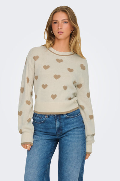 Pull à col rond beige de JDY, à motif cœurs marron porté avec un jean bleu.
