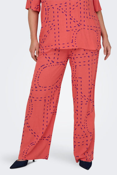 Koraalkleurige broek met geometrisch patroon van CARMAKOMA, gedragen met een bijpassend topje en zwarte pumps.