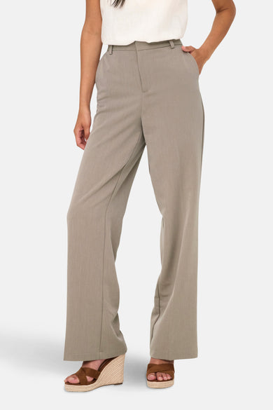 Beige kostuumbroek van ONLY, gedragen met een witte top met ruches en sleehakken.