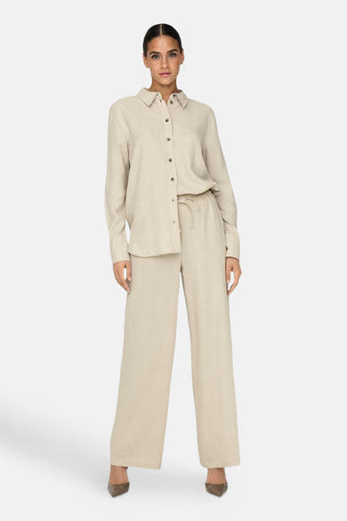 Chemise à manches longues beige de JDY, portée avec un pantalon ample assorti et des escarpins.
