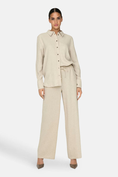 Chemise à manches longues beige de JDY, portée avec un pantalon ample assorti et des escarpins.
