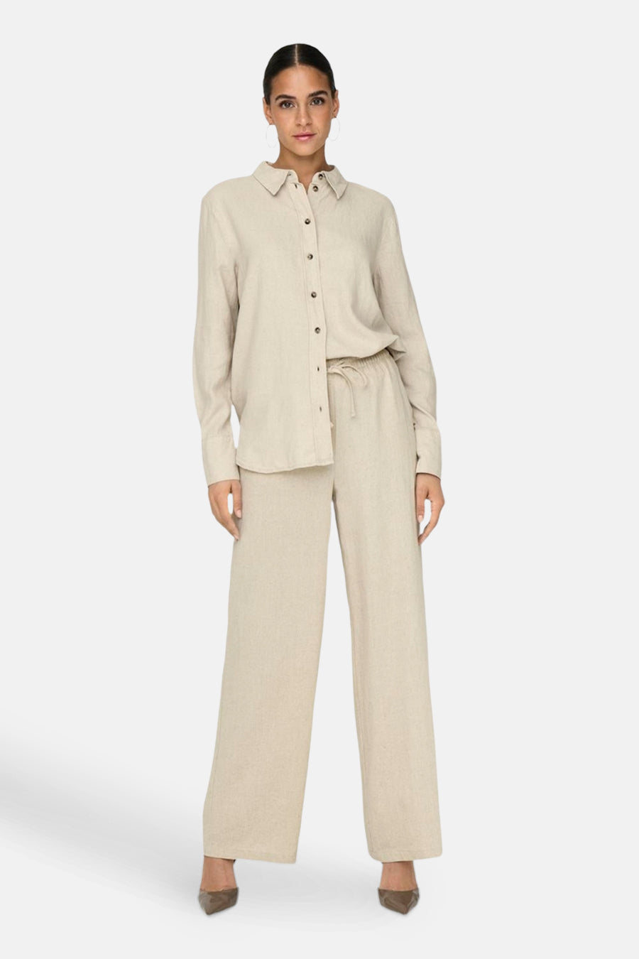 Chemise à manches longues beige de JDY, portée avec un pantalon ample assorti et des escarpins.
