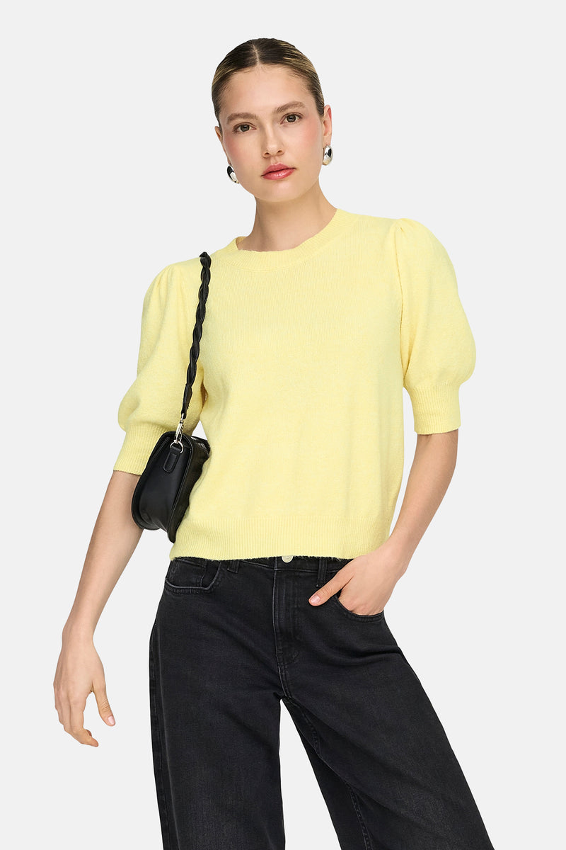 Pull à col rond jaune de ONLY®, manches bouffantes, porté avec un jean noir et un sac à main noir.
