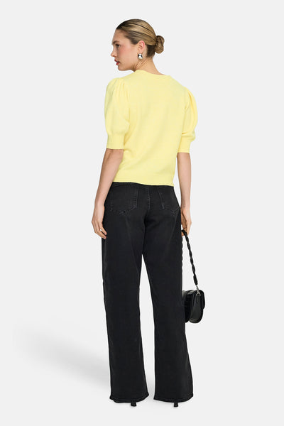 Pull à col rond jaune de ONLY®, avec des manches courtes bouffantes et porté avec un jean noir ample et un sac à main noir.
