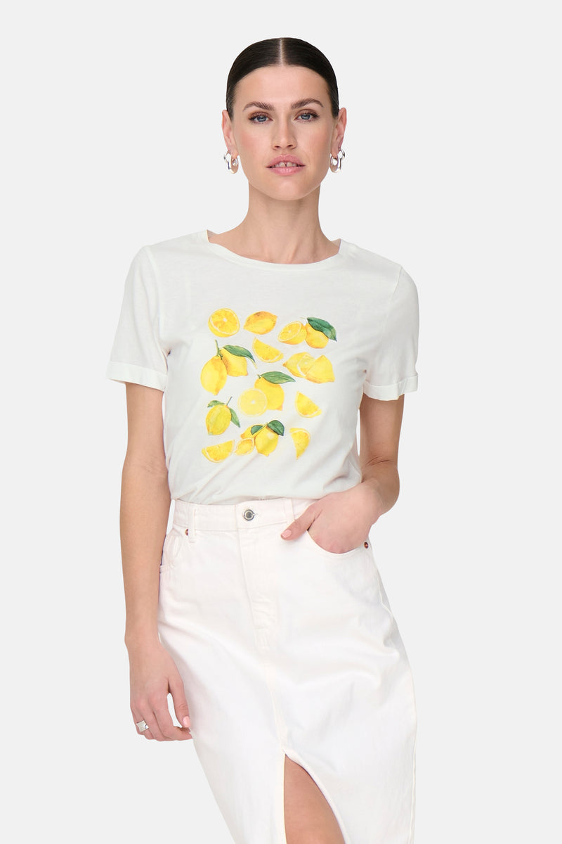 T-shirt blanc à manches courtes de JDY, orné d'un motif citron coloré, porté avec une jupe blanche fendue.
