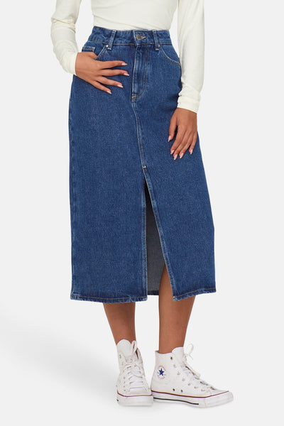 Jupe midi en jean bleu de ONLY, avec fente avant et portée avec des baskets blanches.