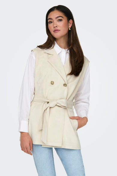 Beige mouwloos vest van ONLY, gedragen over een wit overhemd en een lichtblauwe jeans, met zwarte enkellaarsjes.
