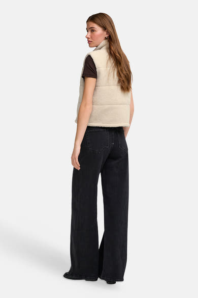 Cream-colored shearling bodywarmer with quilted panels and high collar, side view on model wearing dark brown top and black wide-leg jeans