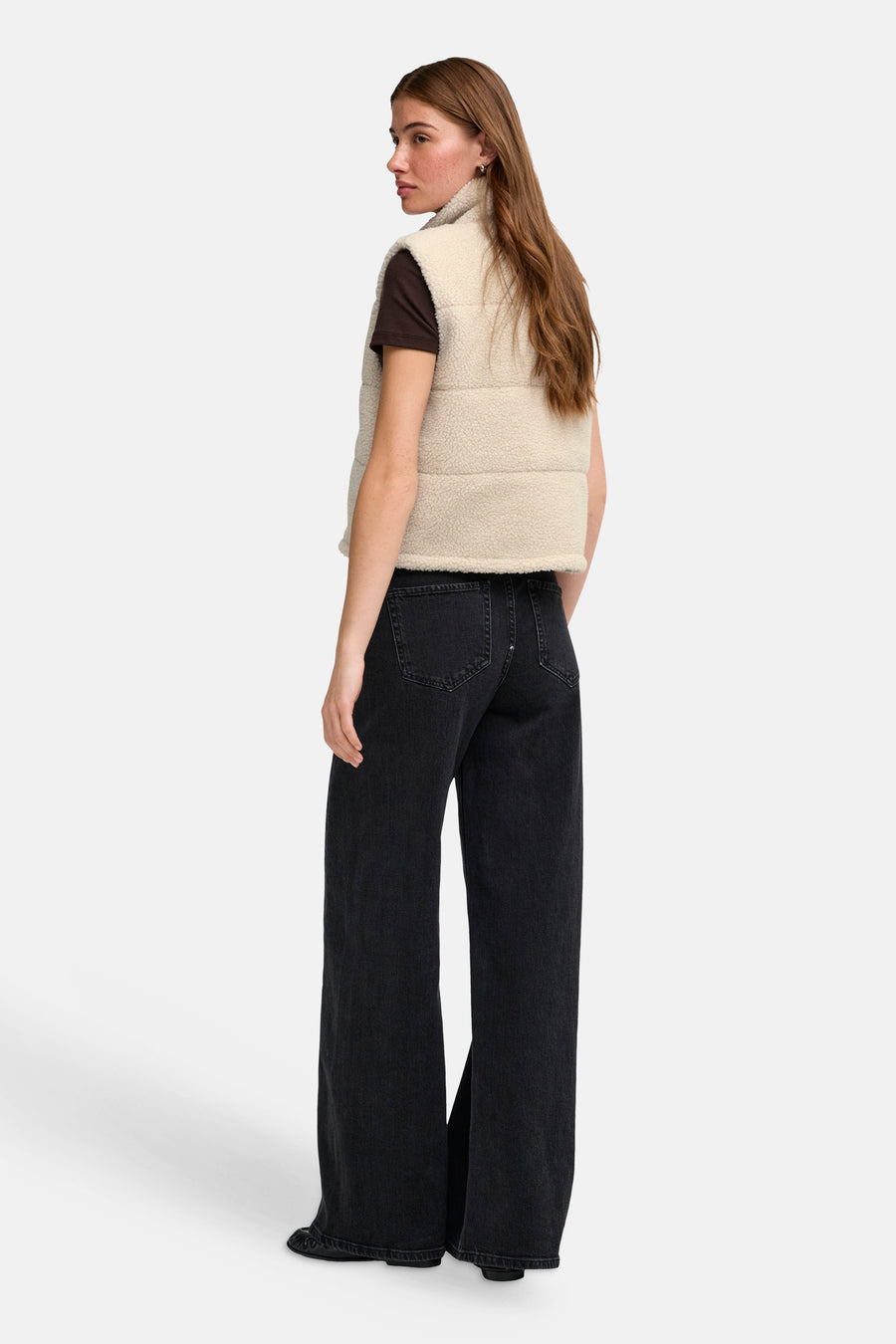 Cream-colored shearling bodywarmer with quilted panels and high collar, side view on model wearing dark brown top and black wide-leg jeans