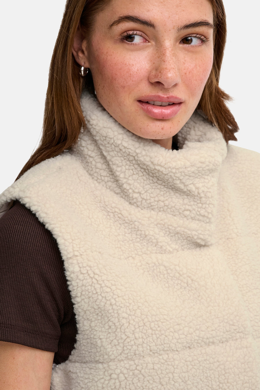 Pumice stone shearling bodywarmer with high cowl neck, worn over dark ribbed top, close-up side view